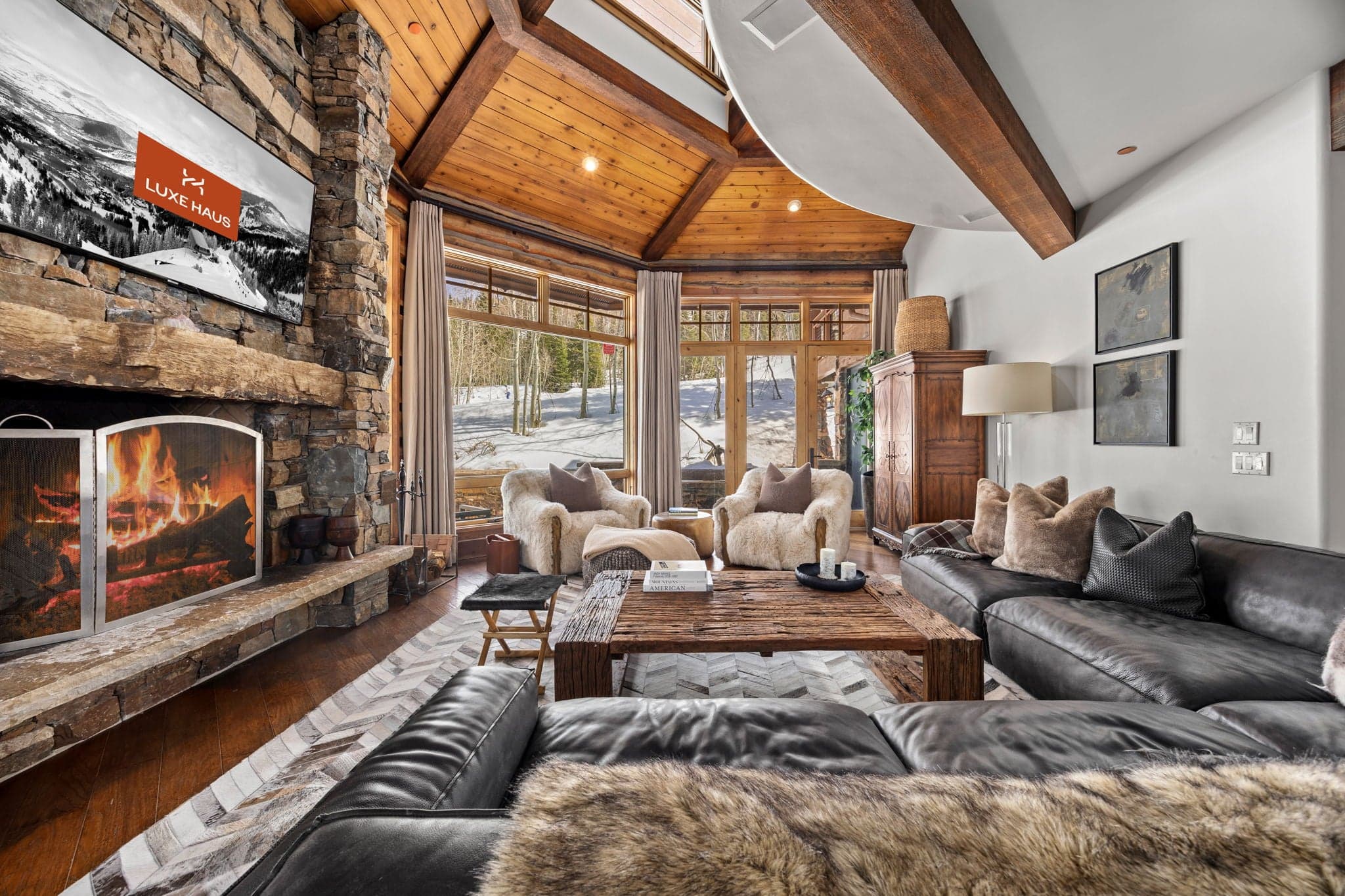a view of the living room with large windows and views of the slopes. there is a screen saver on the TV that says Luxe Haus